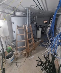Technikraum im Rohbau mit Leiter, Speicher und offen verlegten Leitungen