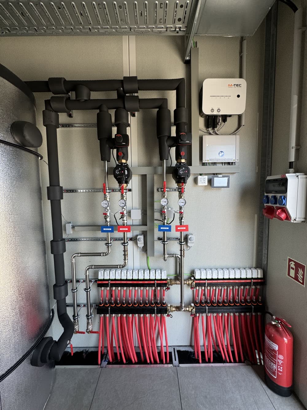 Heizkreisverteiler mit roten Leitungen, Pumpen und Regler in einer [tecbox]